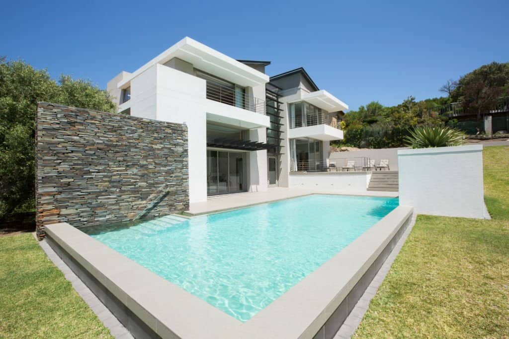 a large inground pool outside a white two-story modern house surrounded by landscaping