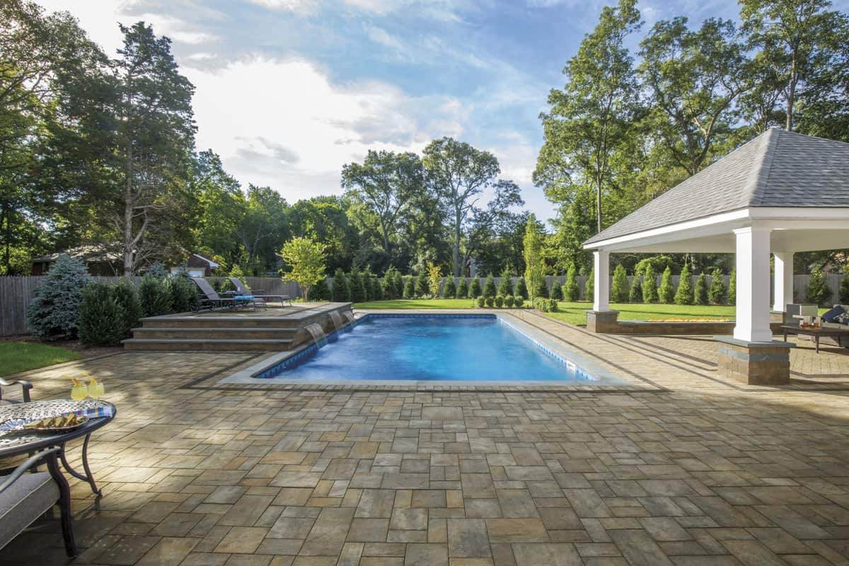 a rectangular inground pool on a paver patio next to a white pergola