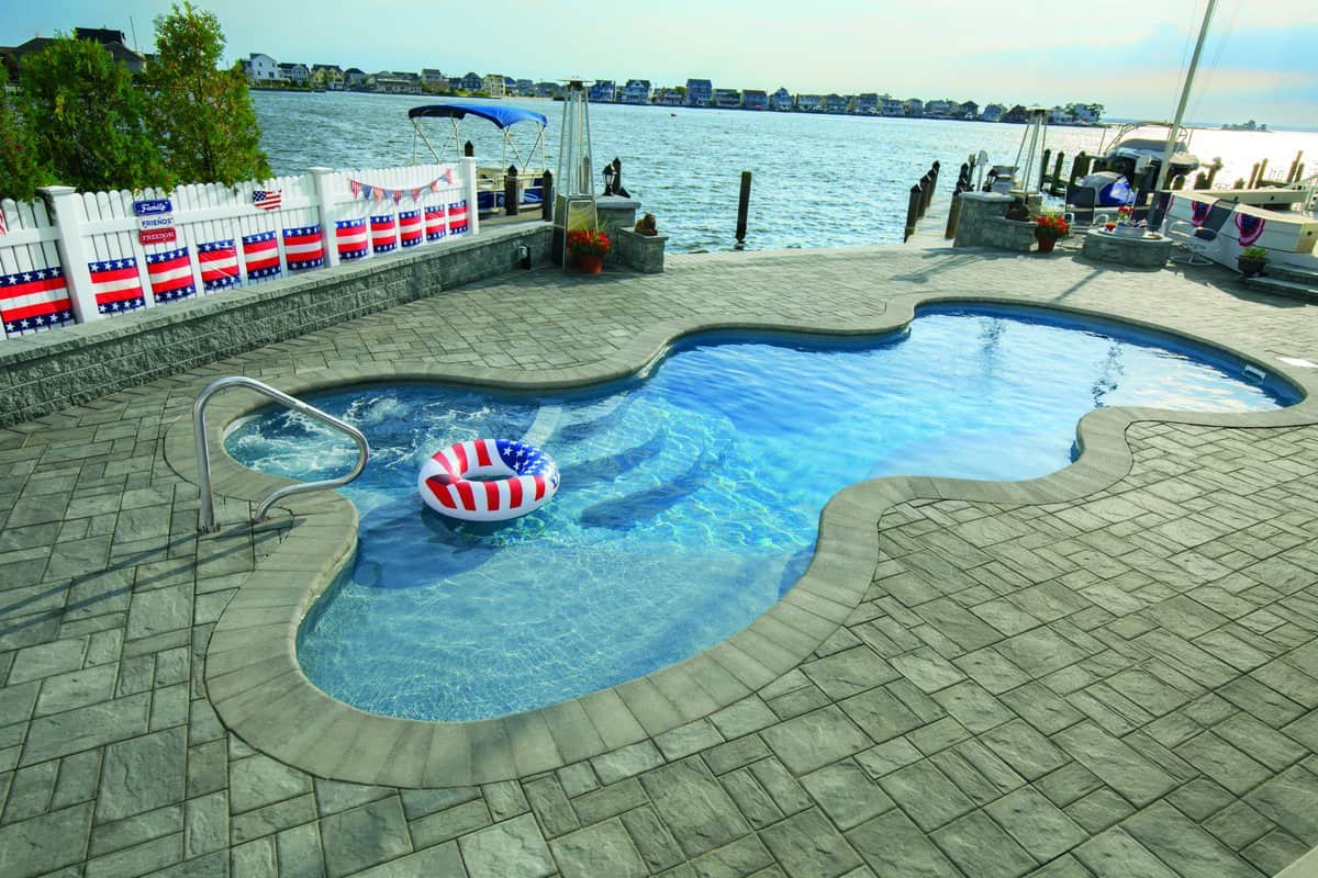 an inground swimming pool on a dock looking over a lake with a bridge in the distance